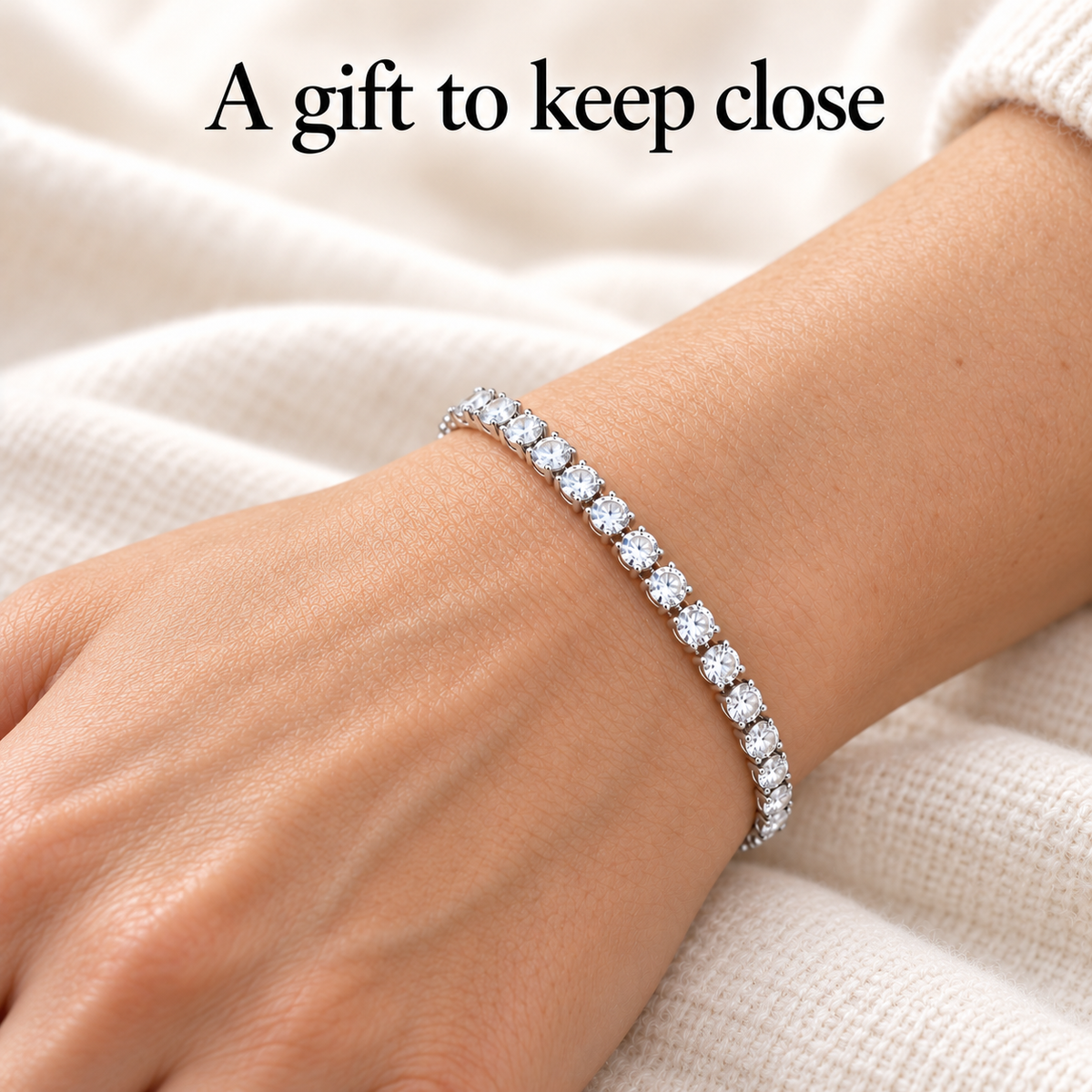 Tennis bracelet worn on a wrist, showing a delicate row of clear stones beside a cream knitted sleeve.