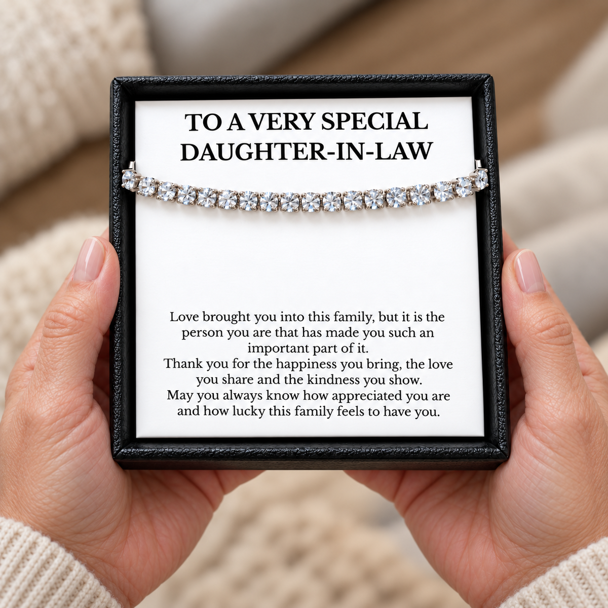 Hands holding a black gift box containing a tennis bracelet and daughter-in-law message card.