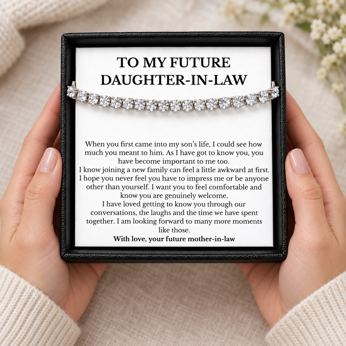 Hands holding a black gift box with a tennis bracelet and a welcoming message for a future daughter-in-law.
