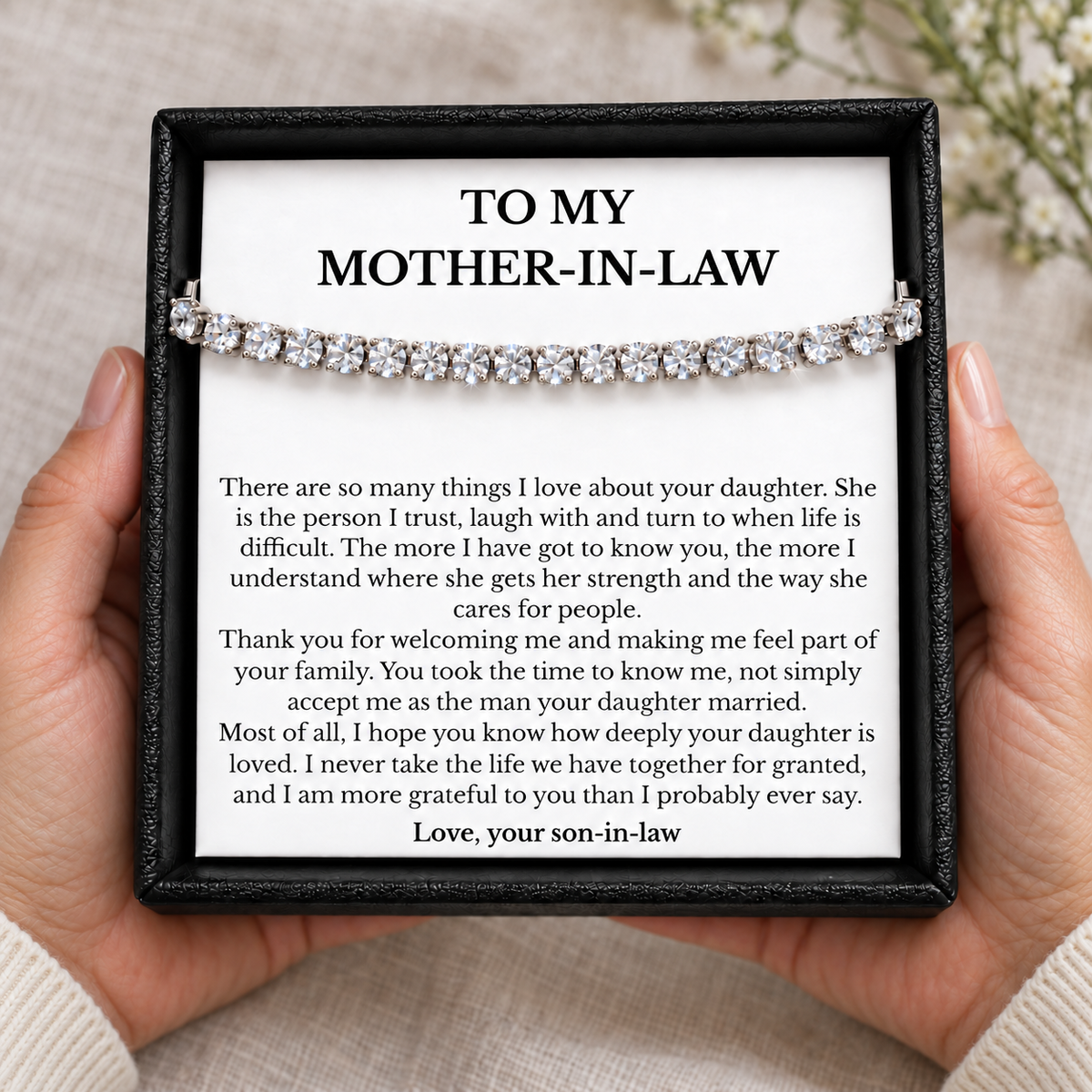 Hands holding an open black gift box containing a tennis bracelet and a heartfelt mother-in-law card from her son-in-law.
