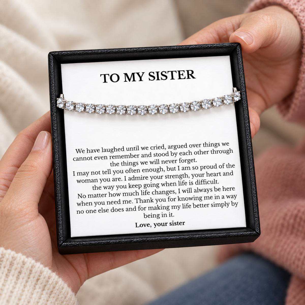 Hands holding a black gift box containing a tennis bracelet and a To My Sister message card.