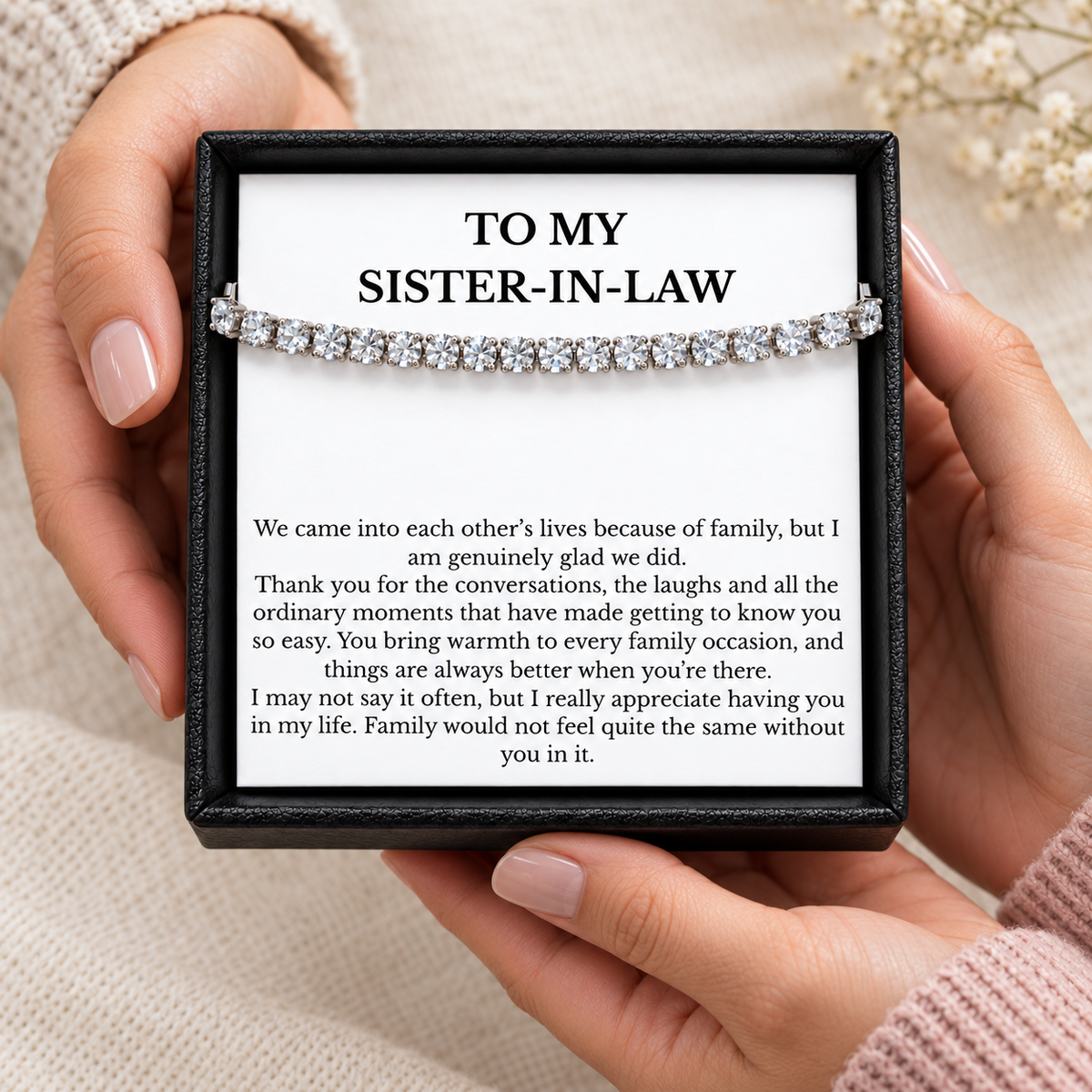 Hands holding an open black gift box containing a tennis bracelet and heartfelt sister-in-law message card.