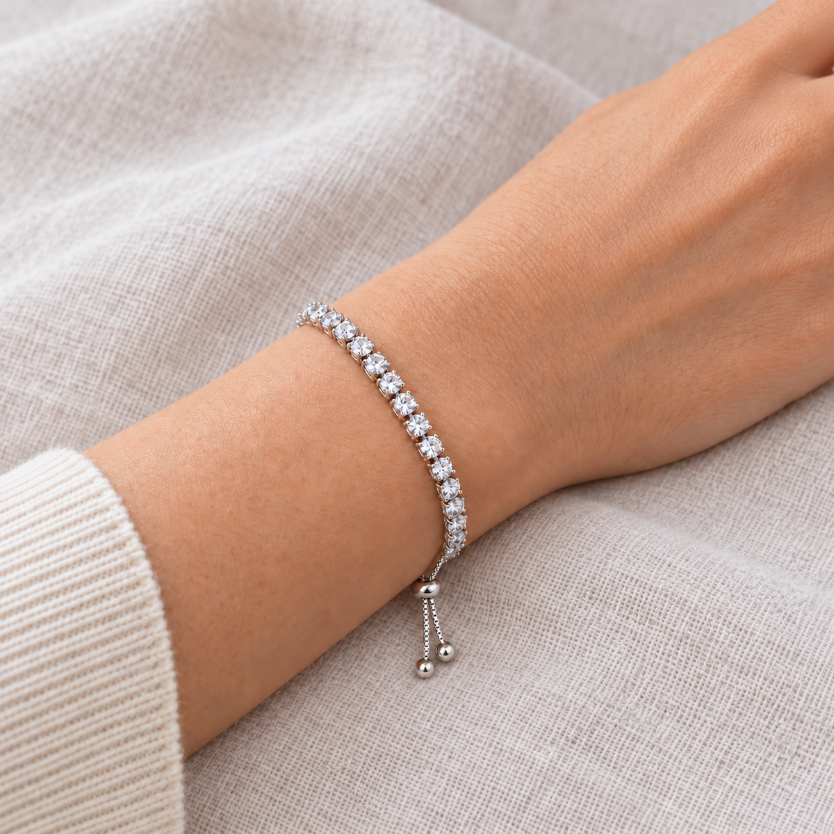 Silver-coloured tennis bracelet worn on a wrist, showing clear stones, adjustable slider and beaded chain ends.
