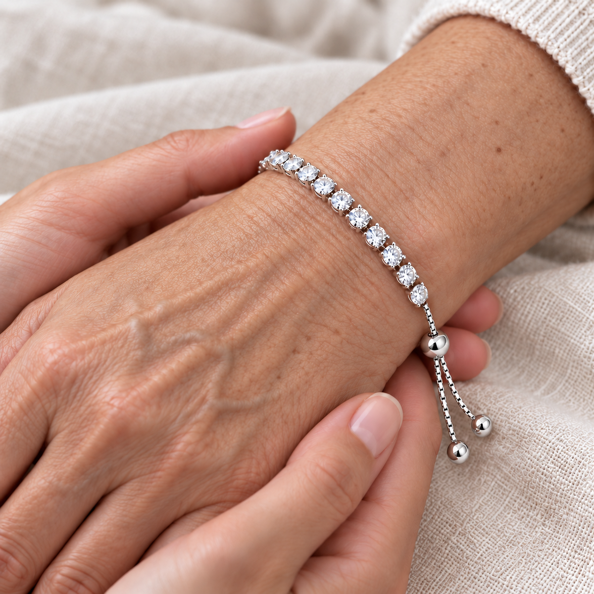 Silver-tone tennis bracelet worn on a wrist, showing its row of clear stones and sliding adjuster.