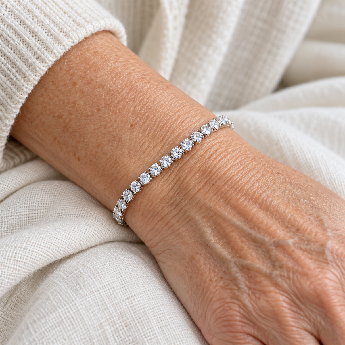 Silver-colour tennis bracelet with a row of clear stones worn on a wrist.