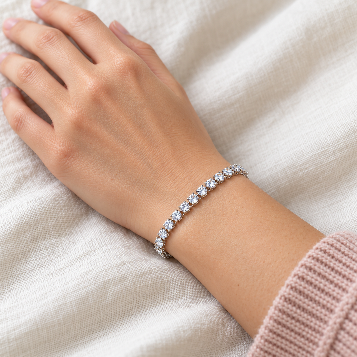 Silver-tone tennis bracelet with a row of clear stones worn on a granddaughter’s wrist beside a soft pink sleeve.