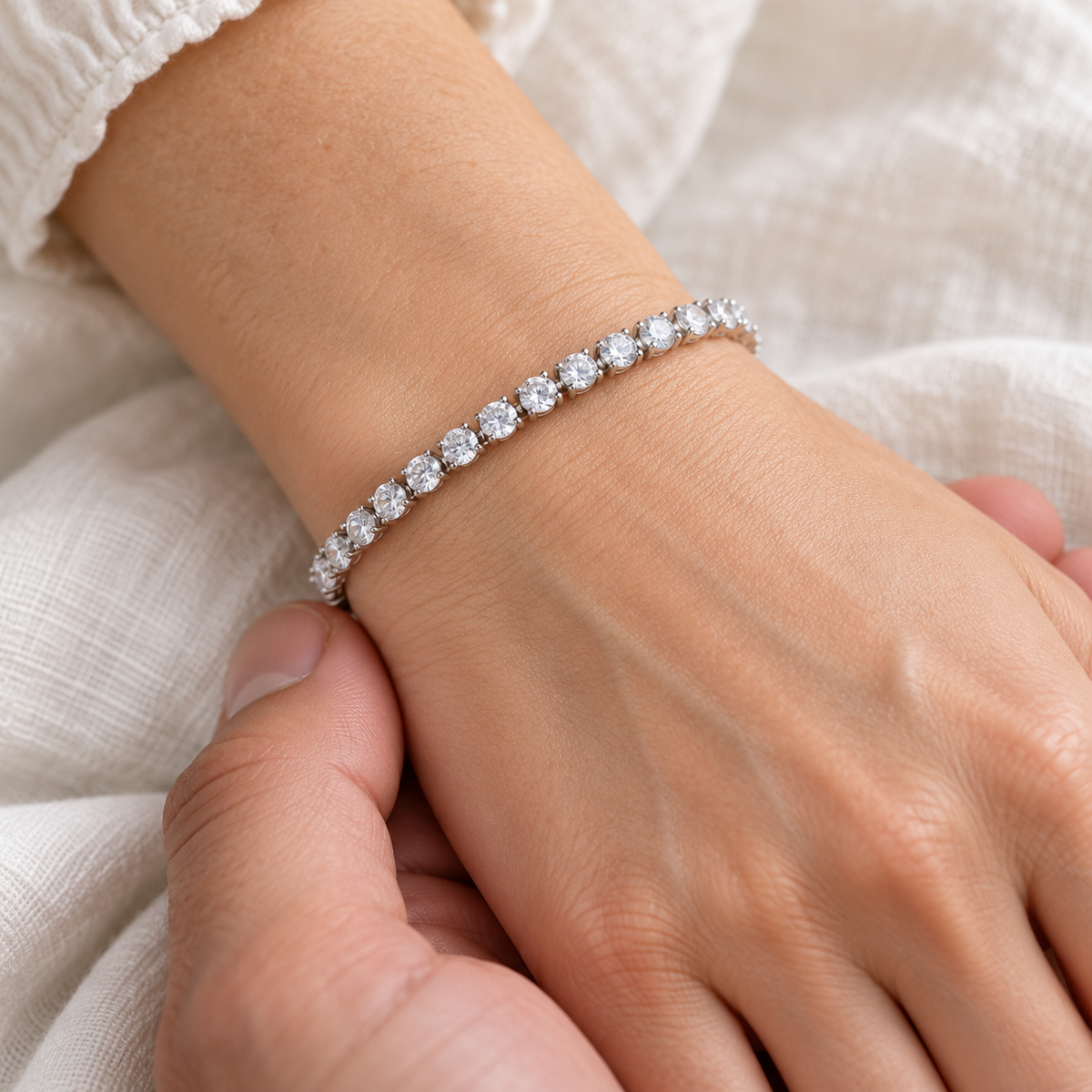 Silver-tone tennis bracelet with clear stones worn on a wrist.