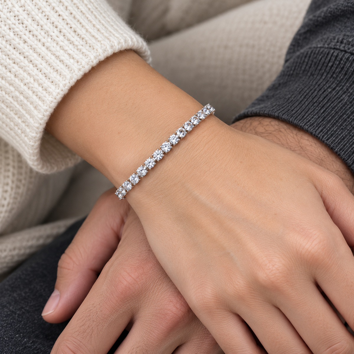 Silver colour tennis bracelet with clear stones worn on a wrist as two people hold hands.