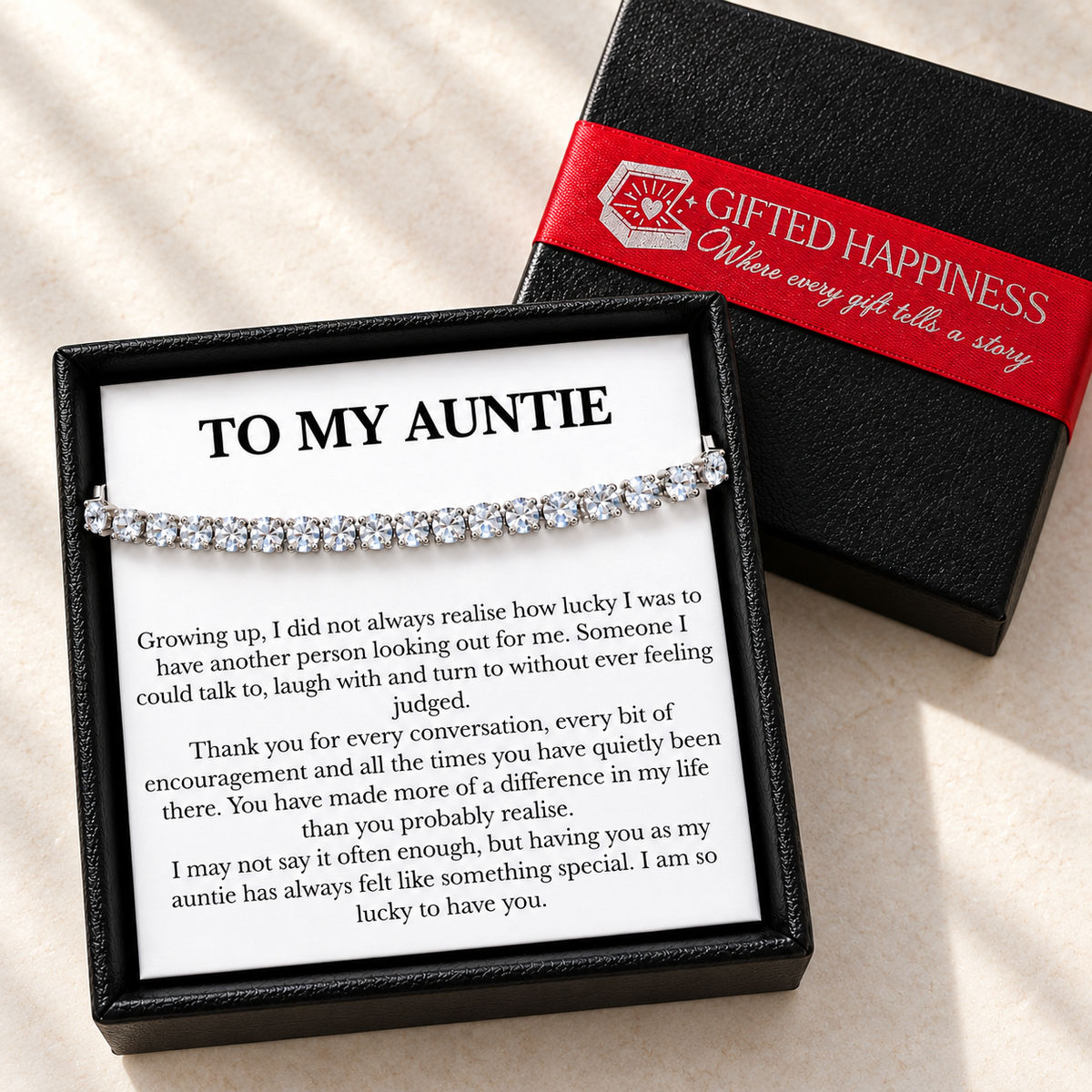 Auntie bracelet and heartfelt message card in an open black gift box beside its lid with Gifted Happiness red ribbon.