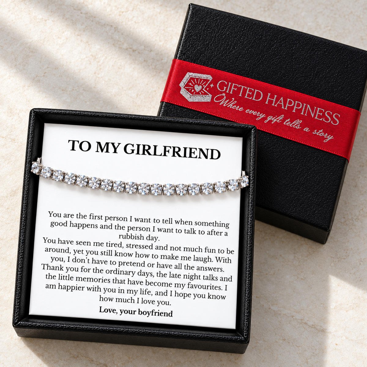 Girlfriend tennis bracelet and message card in an open black gift box beside its lid with red Gifted Happiness ribbon.