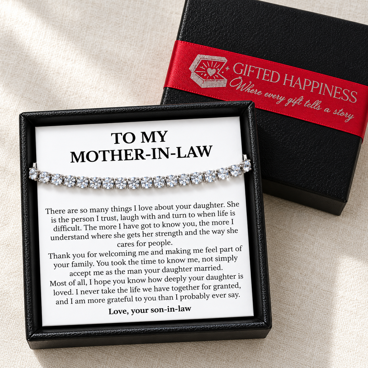 Tennis bracelet and mother-in-law message card beside a black box lid wrapped with Gifted Happiness red ribbon.
