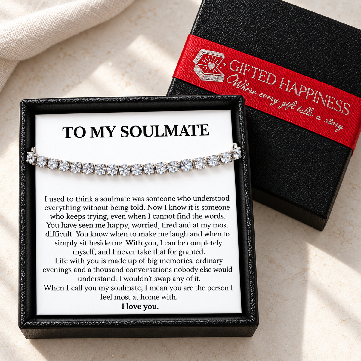 Soulmate tennis bracelet and message card in an open black gift box beside the lid with a red Gifted Happiness ribbon.