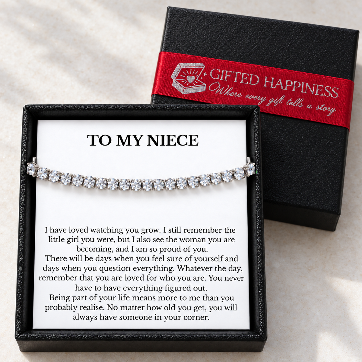 Niece tennis bracelet and message card in an open black gift box beside its lid with a red Gifted Happiness ribbon.
